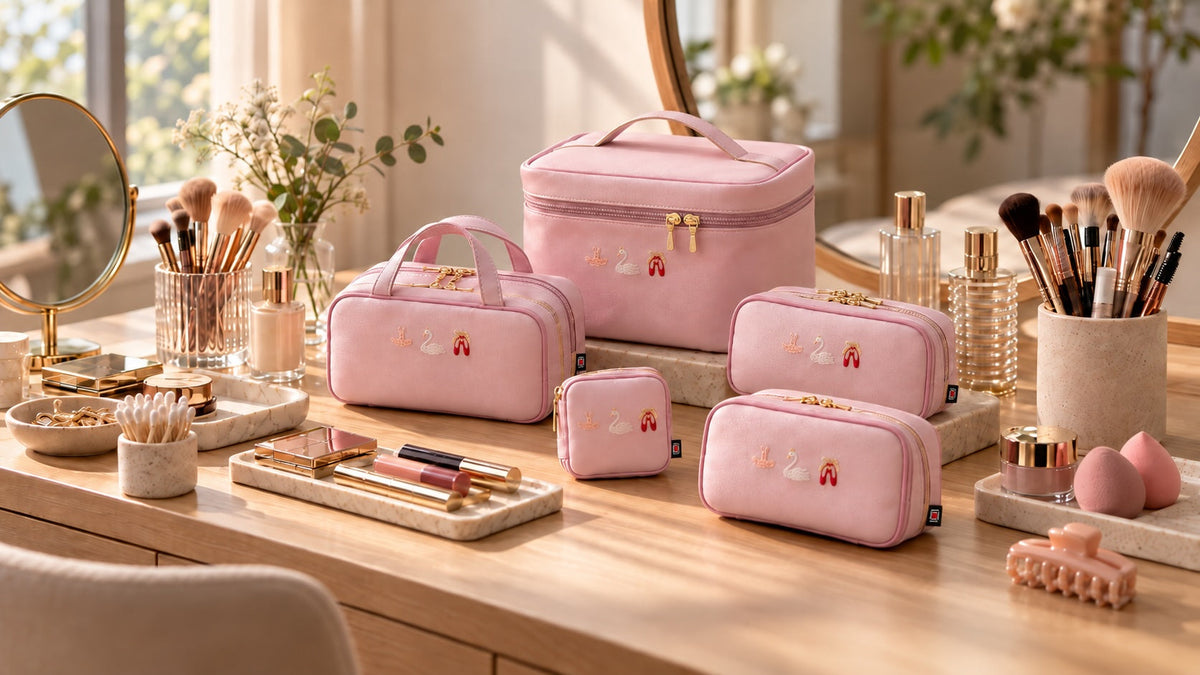 Five pink makeup pouches in different sizes arranged on a vanity table with makeup brushes and cosmetics.